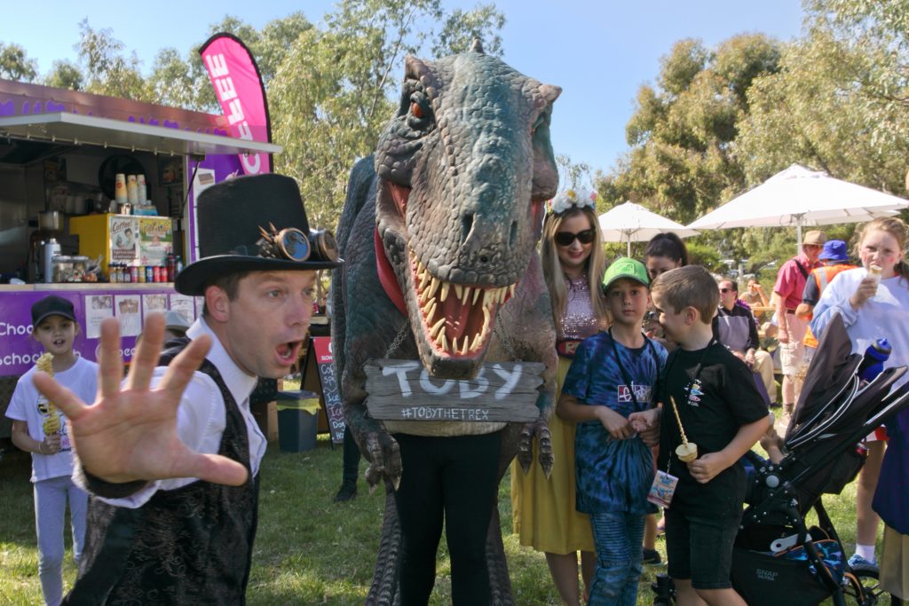 photo showing children with a big dinosaur puppet in front of a food truck