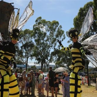 image of a scene from the community festival in 2024 with stilt performers dressed like giant bees